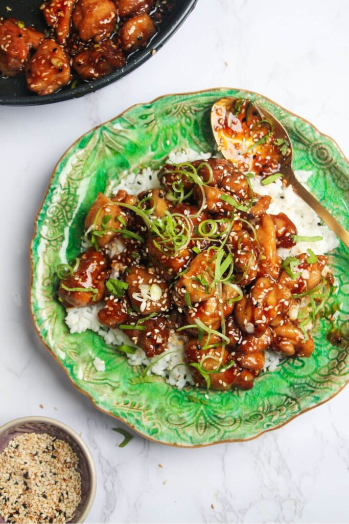 Honey sesame chicken topped with cilantro and scallions with rice on a green plate.