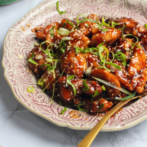 Honey sesame chicken topped with cilantro and scallions on a pink plate.