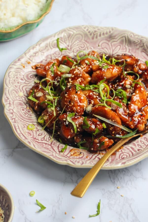 Honey sesame chicken topped with cilantro and scallions on a pink plate.