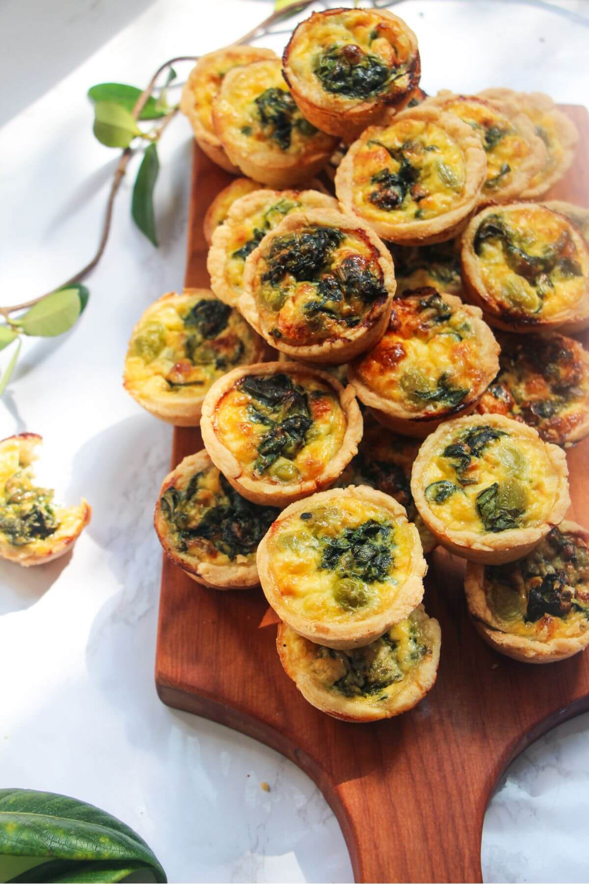 A pile of mini coronation quiches on a small wooden board.