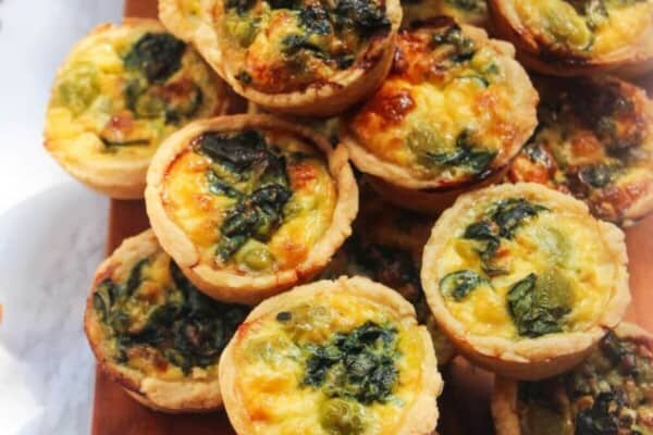 A pile of mini coronation quiches on a small wooden board.