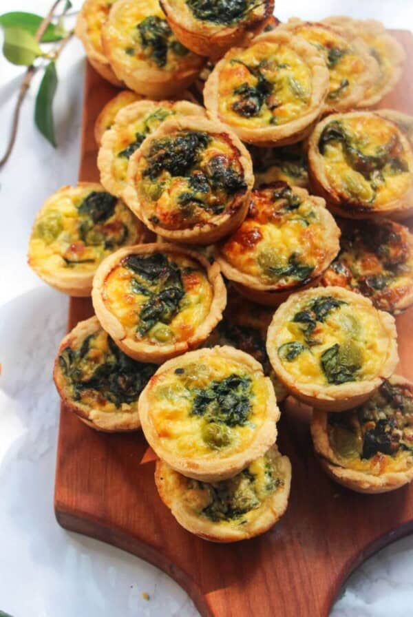 A pile of mini coronation quiches on a small wooden board.