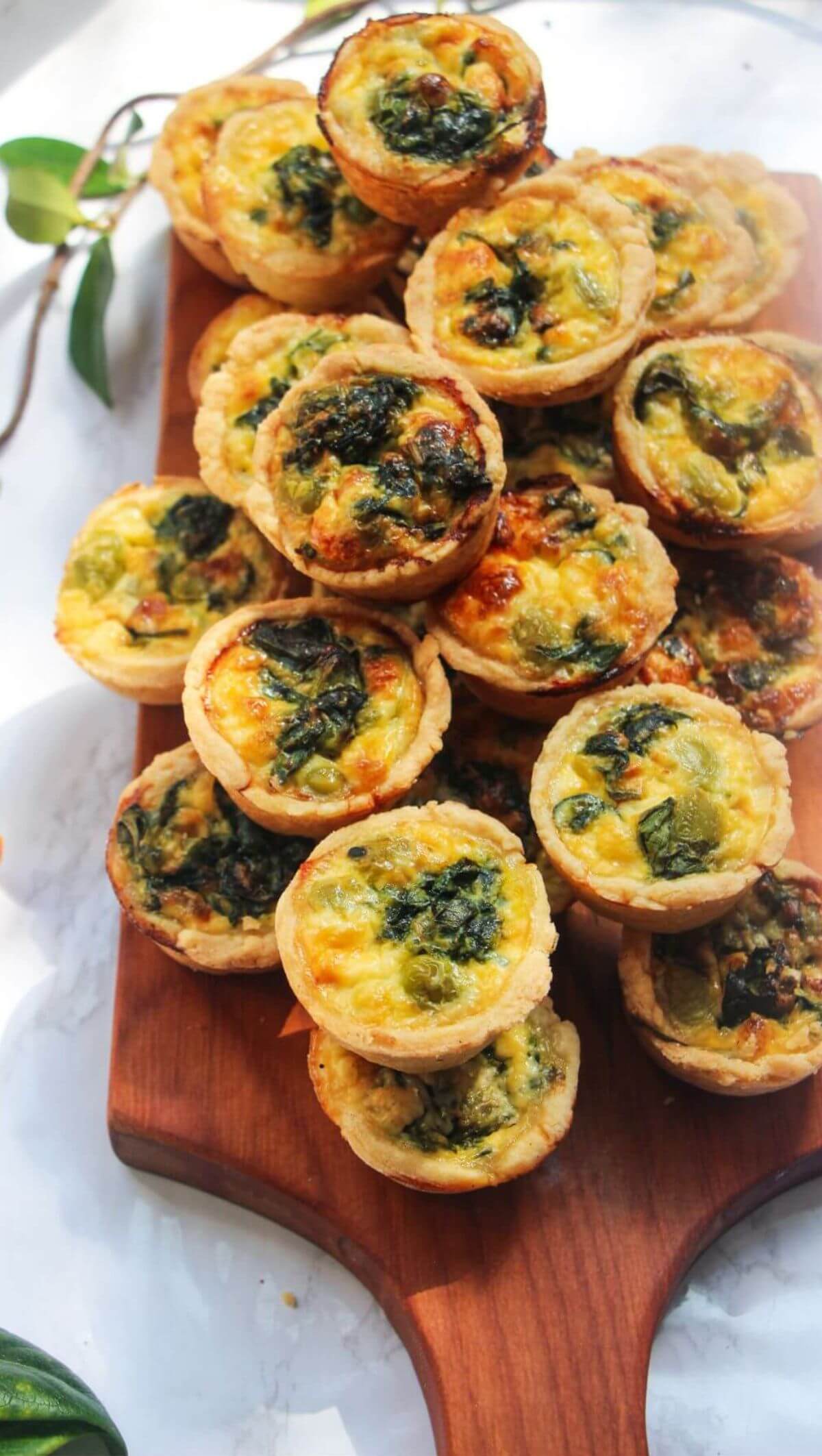 A pile of mini coronation quiches on a small wooden board.