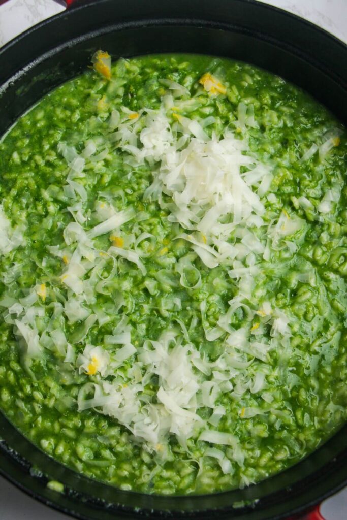 Grated parmesan on top of wild garlic risotto in a large black skillet.