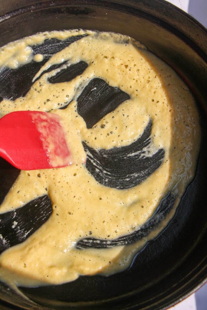 Red spatula mixing roux in a large black pan.