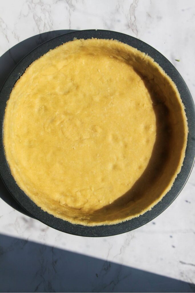 Pastry pressed into a small quiche tin on a white background.