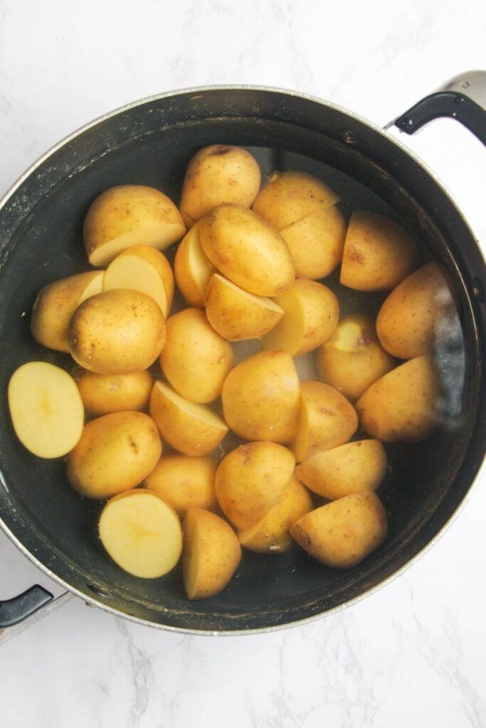 Baby potatoes in a large black pot full of water.