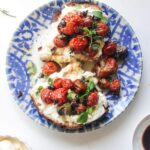 Roasted tomato and burrata toast sliced in half, on a white and blue plate.