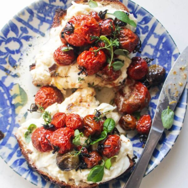 Roasted tomato and burrata toast sliced in half, on a white and blue plate.