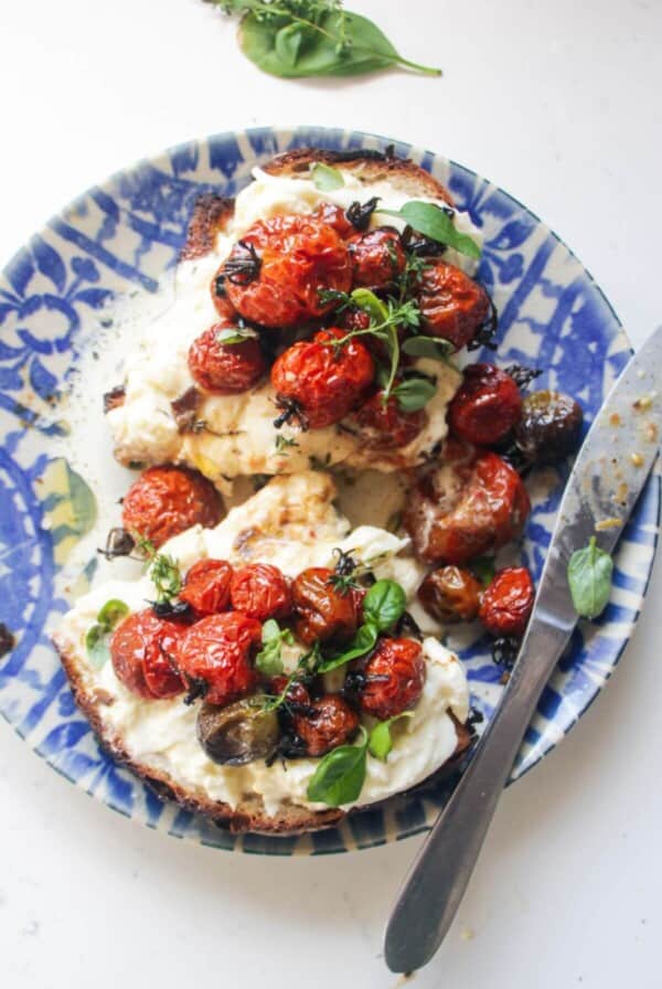 Roasted tomato and burrata toast sliced in half, on a white and blue plate.