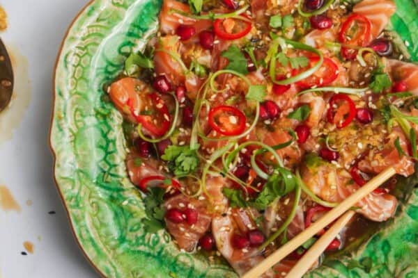Salmon crudo on a small green plate with chopsticks and lime on the side.