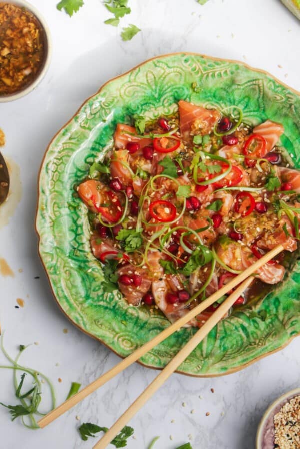 Salmon crudo on a small green plate with chopsticks and lime on the side.