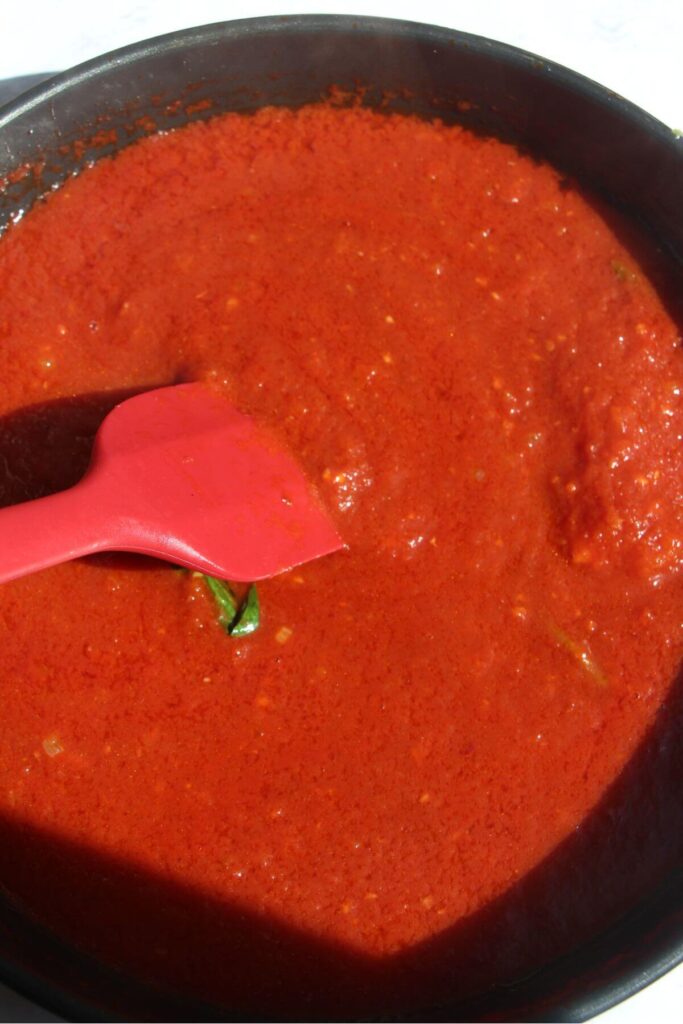 Red spatula stirring thickened tomato sauce in a small frying pan.