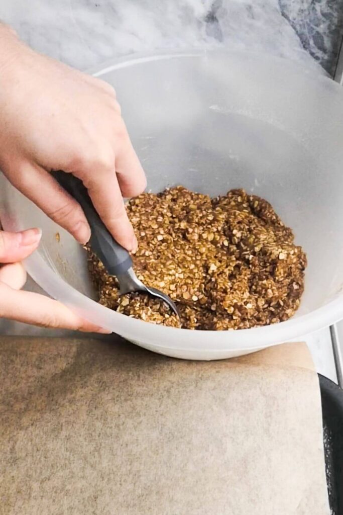 Hand using a cookie scoop to scoop up a ball of Anzac biscuit dough.