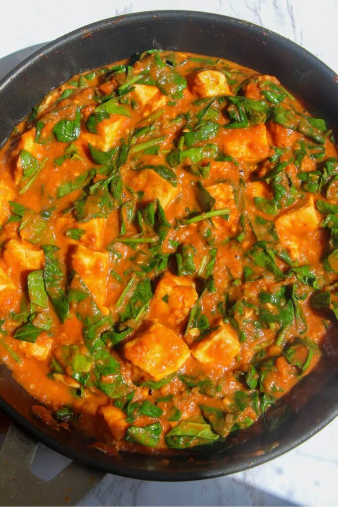 Spinach stirred through halloumi curry in a small frying pan.