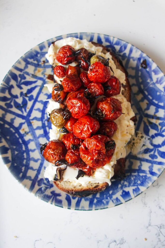 Roasted cherry tomatoes piled on top of burrata on a piece of toast.
