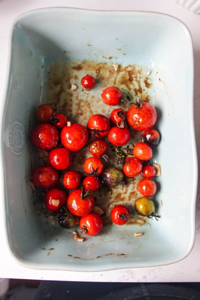 Cherry tomatoes, garlic, olive oil and balsamic vinegar in a small blue baking dish.