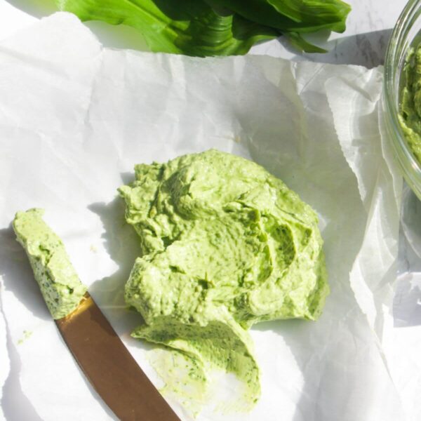 Wild garlic butter on a piece of baking paper with more wild garlic butter in a small glass bowl, with a gold knife on the side.