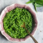 Bright green wild garlic pesto in a small pink bowl on a grey marble background.