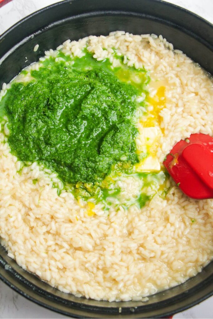 Wild garlic puree and butter added to cooked risotto in a large black skillet.