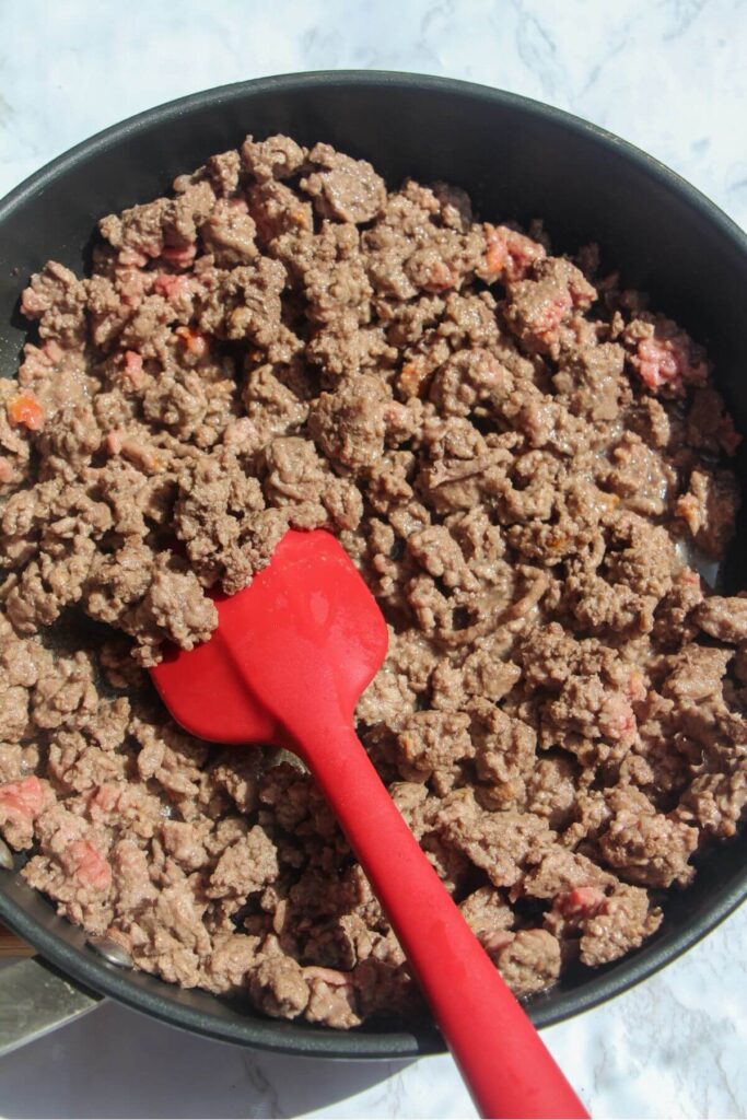 Browned ground beef in a frying pan with a red spatula stirring.