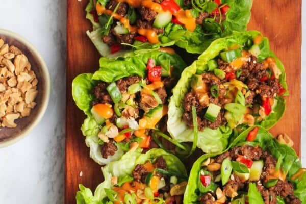 Five Korean beef lettuce wraps on a wooden board.
