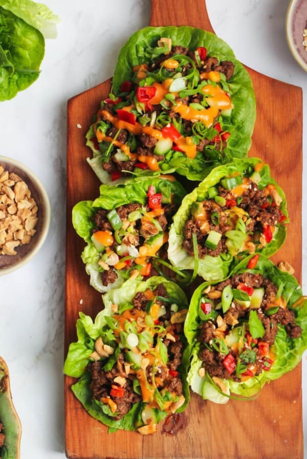 Five Korean beef lettuce wraps on a wooden board.