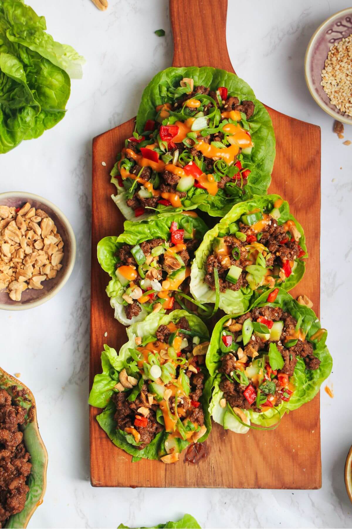 Five Korean beef lettuce wraps on a wooden board.