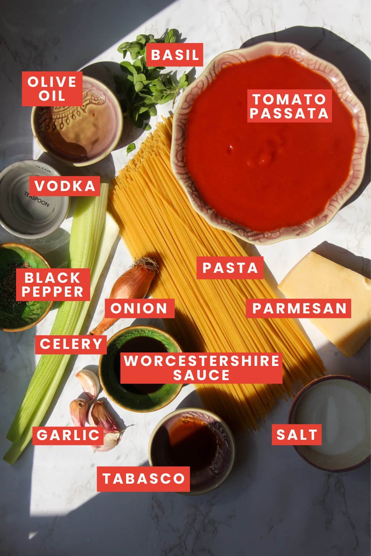 Ingredients for bloody mary pasta laid out on a white marble background and labelled.