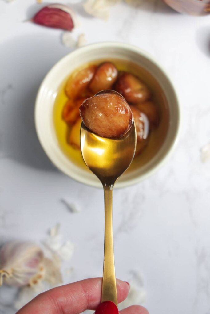 Clove of confit garlic on a small gold spoon.