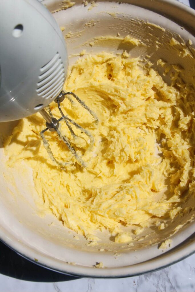 Electric beater creaming butter and sugar in a large white mixing bowl.