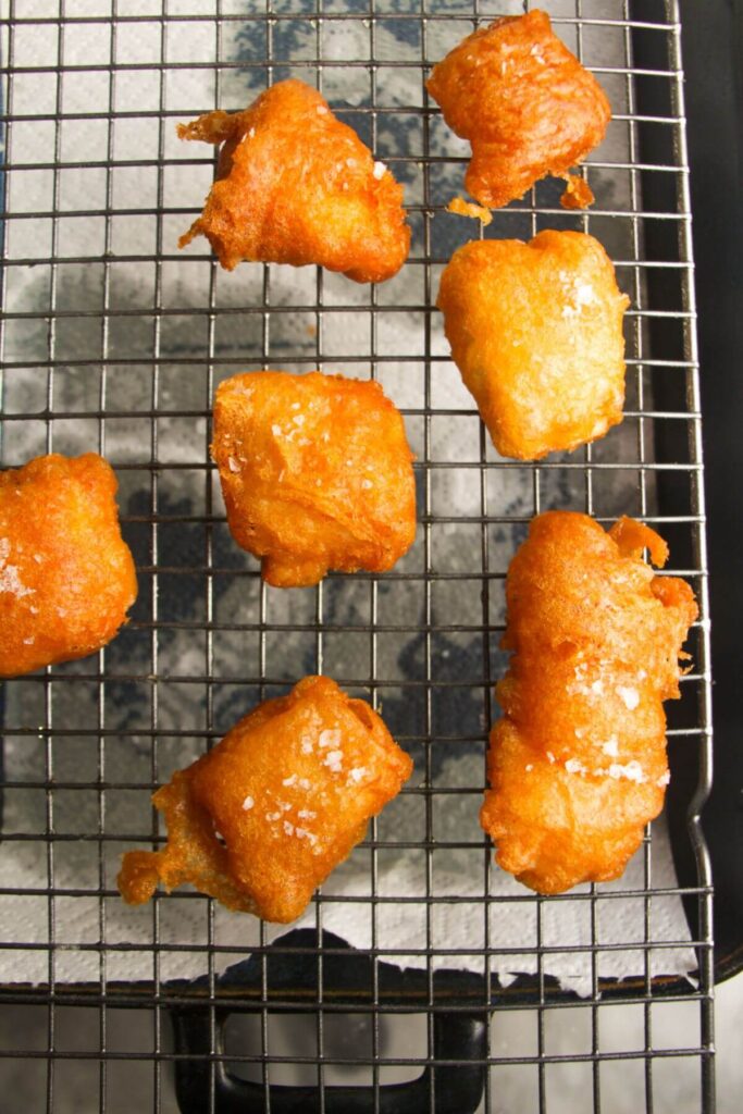 Crispy golden beer battered fish pieces on a wired rack.