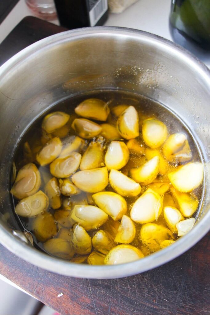 Garlic cloves in olive oil in a small silver pot.