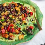 Mexican bean salad on top of whipped avocado on a large green platter.