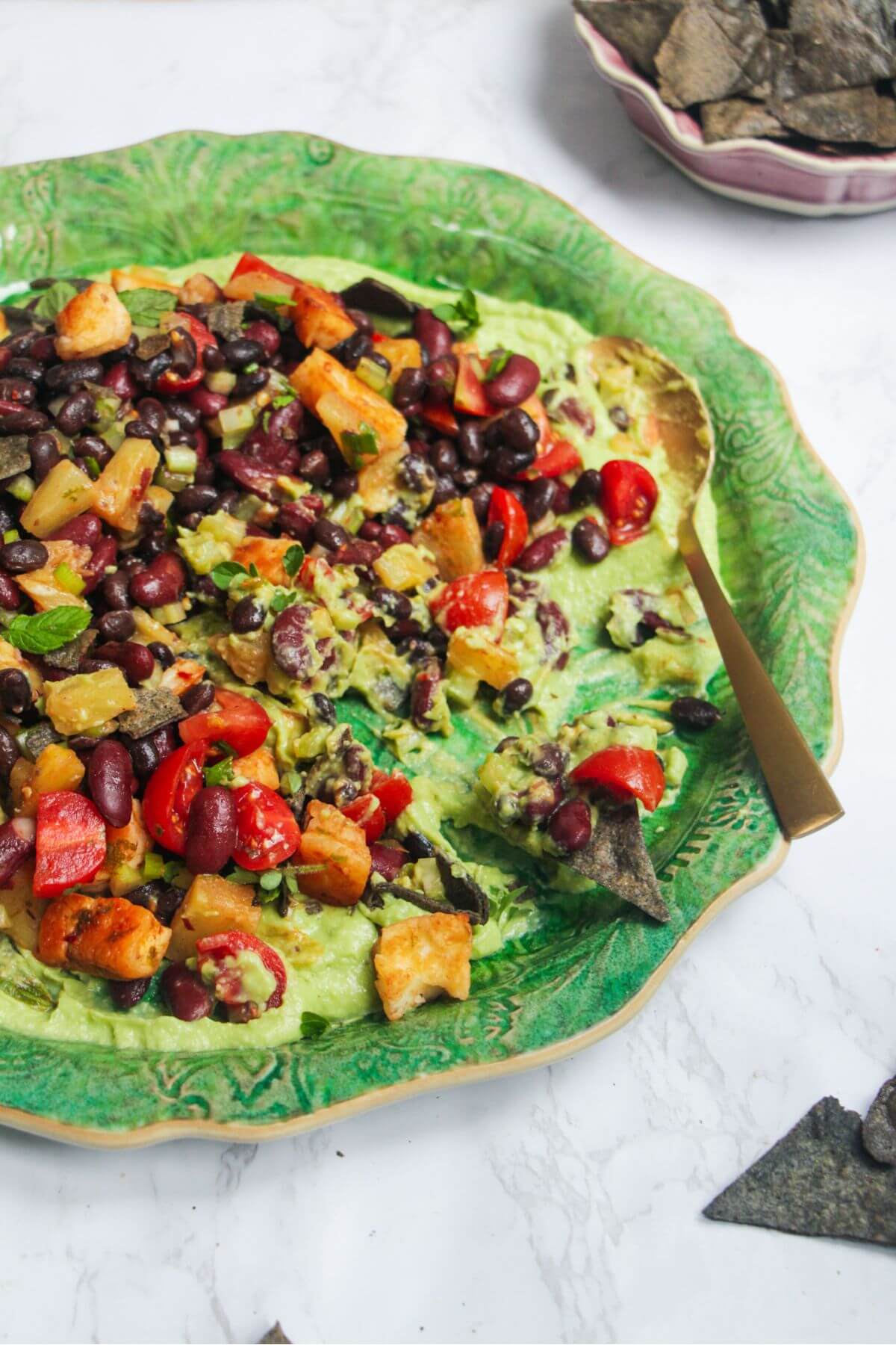 Mexican bean salad on top of whipped avocado on a large green platter.