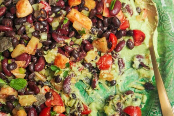 Mexican bean salad on top of whipped avocado on a large green platter.