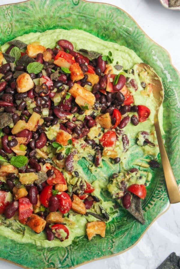 Mexican bean salad on top of whipped avocado on a large green platter.