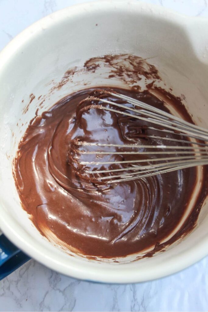 Whisking chocolate icing in a large white bowl.