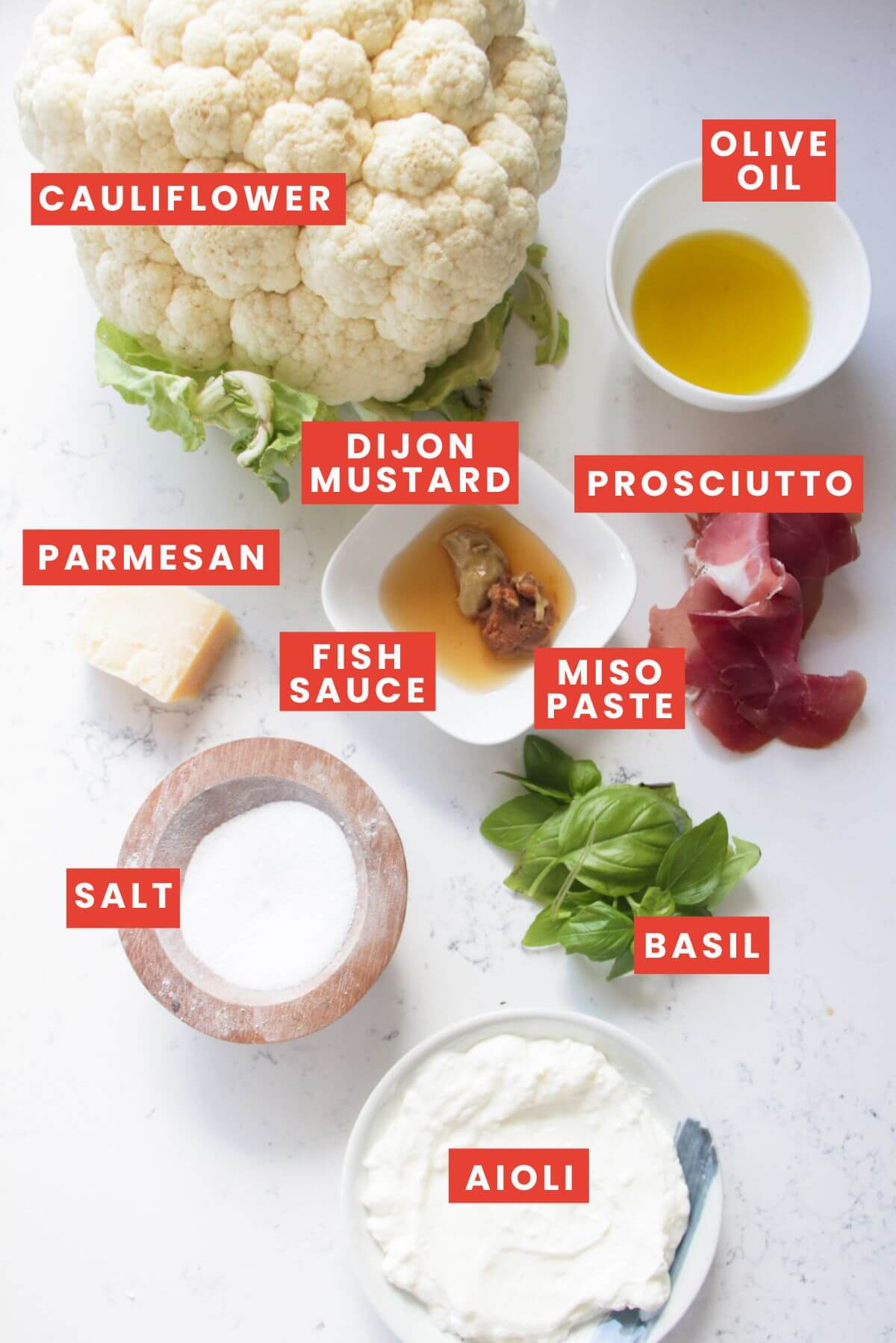 Ingredients for parmesan roasted cauliflower laid out on a white marble background and labelled.