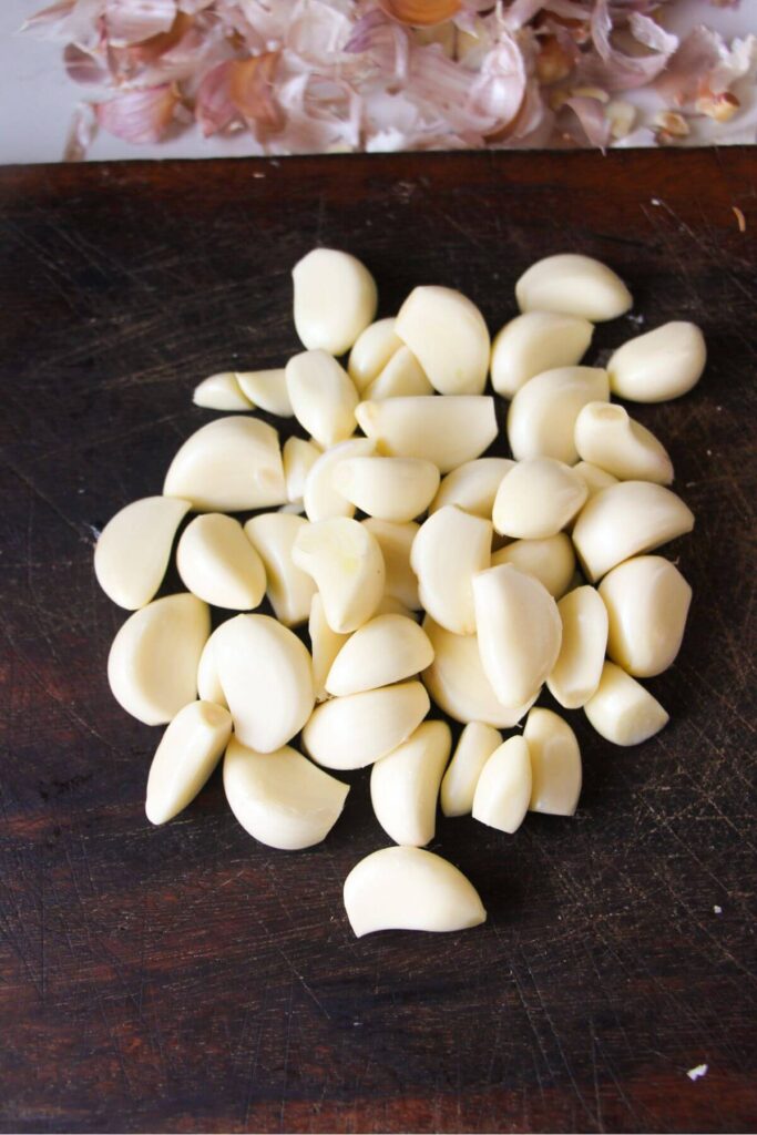 A pile of peeled garlic cloves on a wooden board.