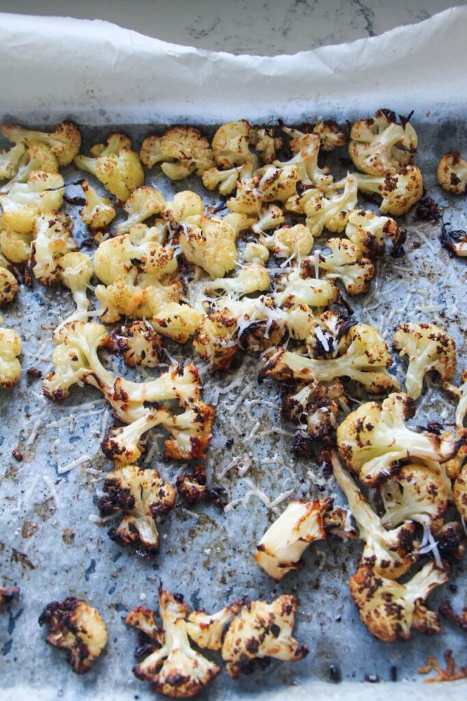 Roasted cauliflower florets on a baking paper lined oven tray.