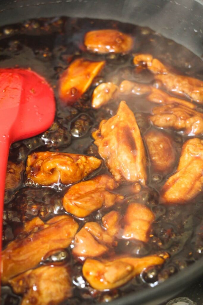 Teriyaki sauce being tossed through chicken in a large frying pan.