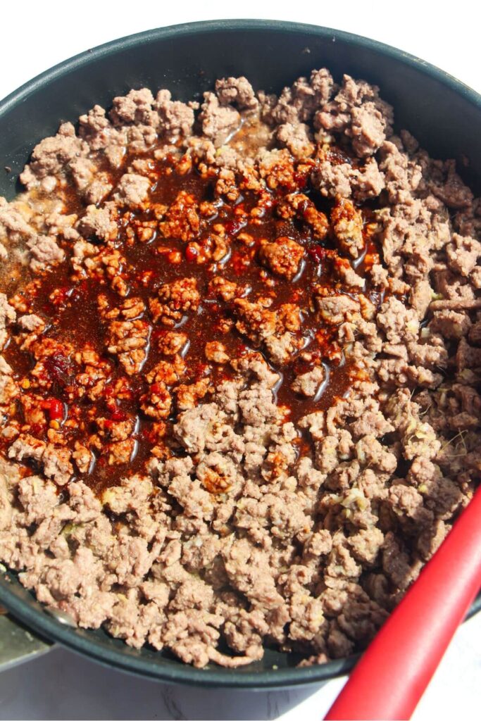 Korean sauce added to cooked, browned ground beef in a pan.