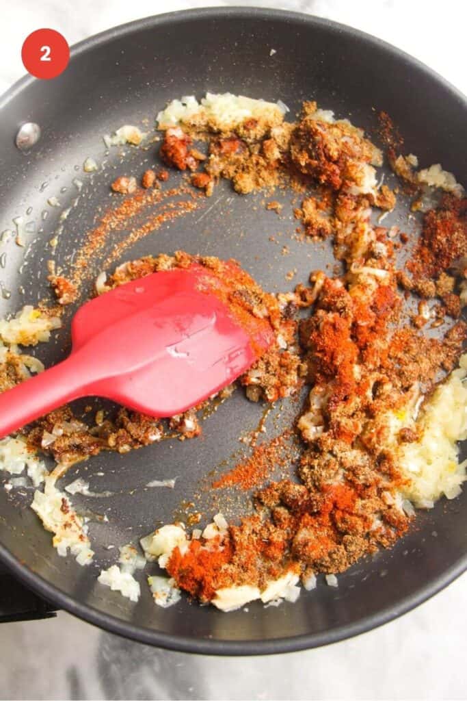 Spatula stirring spices and garlic in a pan.