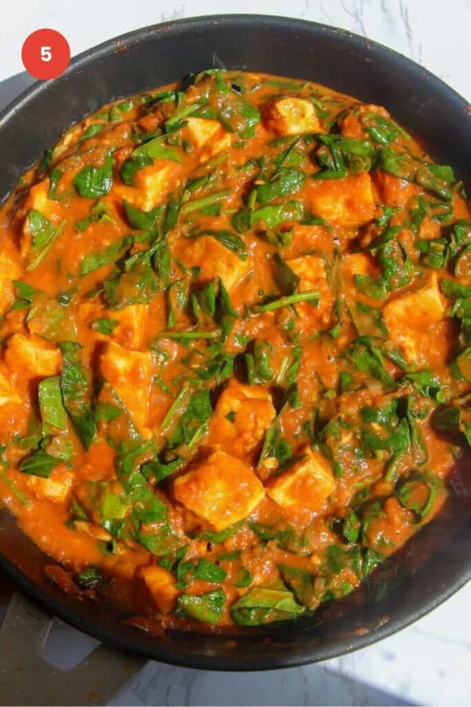 Spinach stirred through halloumi curry in a pan.