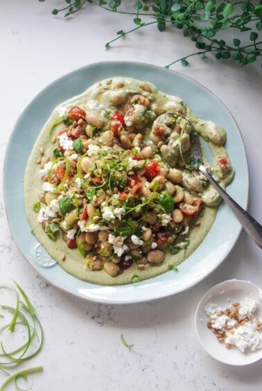 Mediterranean white bean salad on whipped basil tahini on a large light blue serving plate.