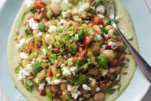Mediterranean white bean salad on whipped basil tahini on a large light blue serving plate.