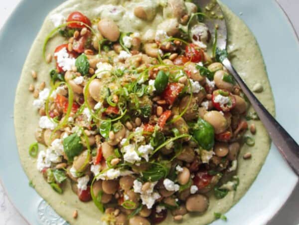 Mediterranean white bean salad on whipped basil tahini on a large light blue serving plate.