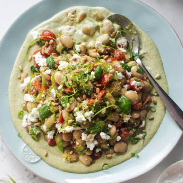 Mediterranean white bean salad on whipped basil tahini on a large light blue serving plate.