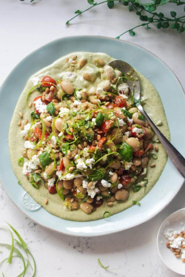Mediterranean white bean salad on whipped basil tahini on a large light blue serving plate.
